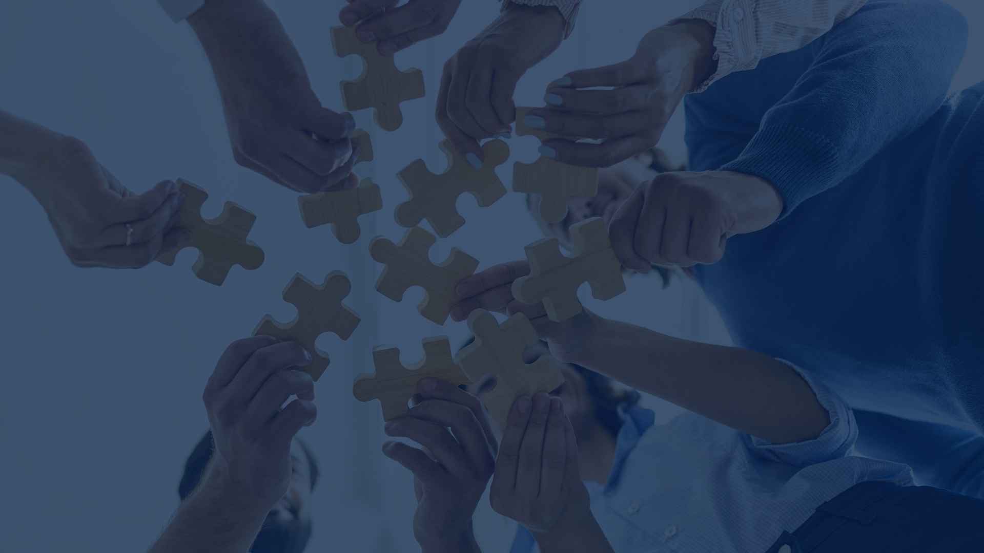 A group of people connecting wooden puzzle pieces symbolising teamwork and collaboration.