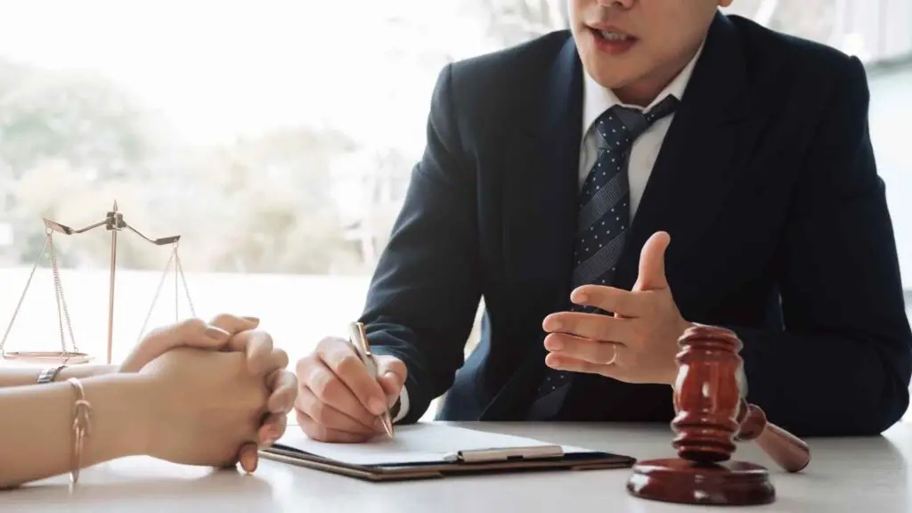 An attorney discusses legal matters with a client, with scales of justice and a gavel on the table.