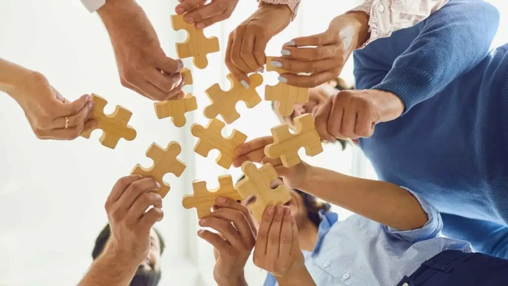 A group of people collaborating, holding wooden puzzle pieces to signify teamwork.