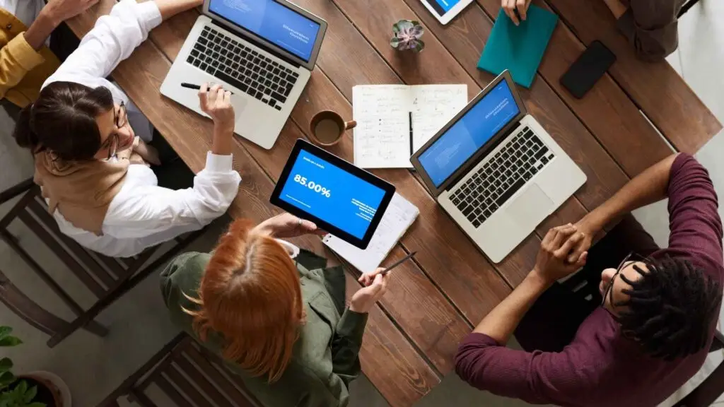 A group of professionals reviewing data insights on tablets and laptops during a collaborative meeting, showcasing digital analytics and teamwork.